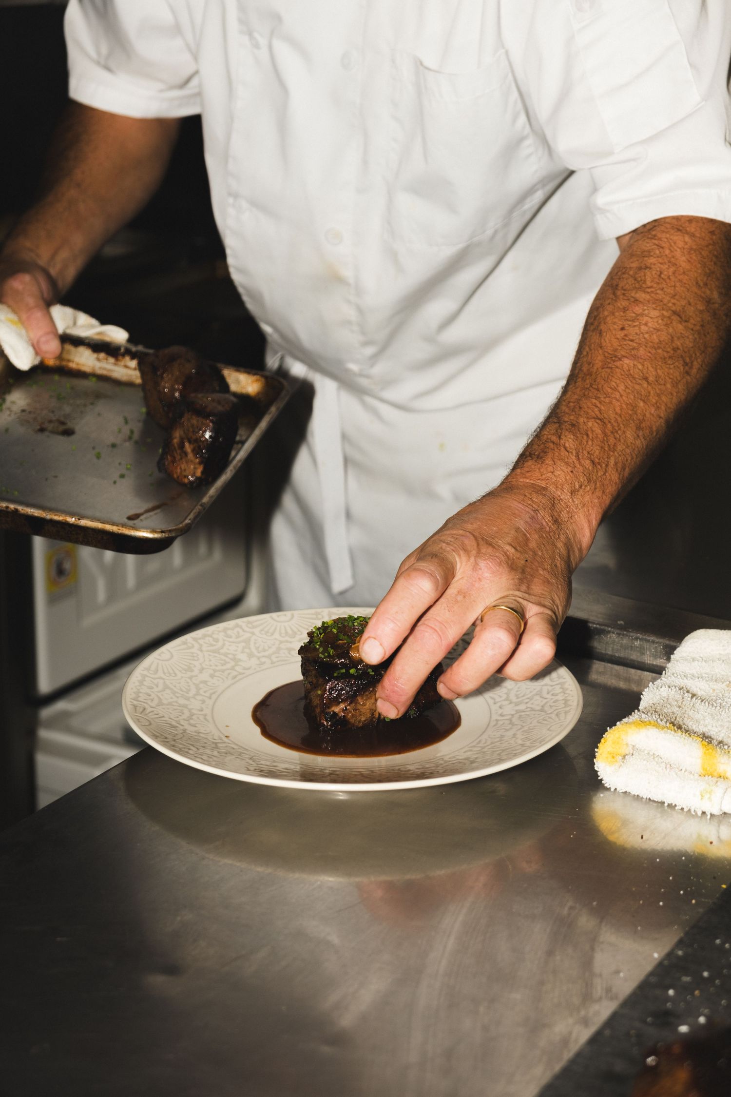 Chef placing food on white plates in a professional kitchen setting.