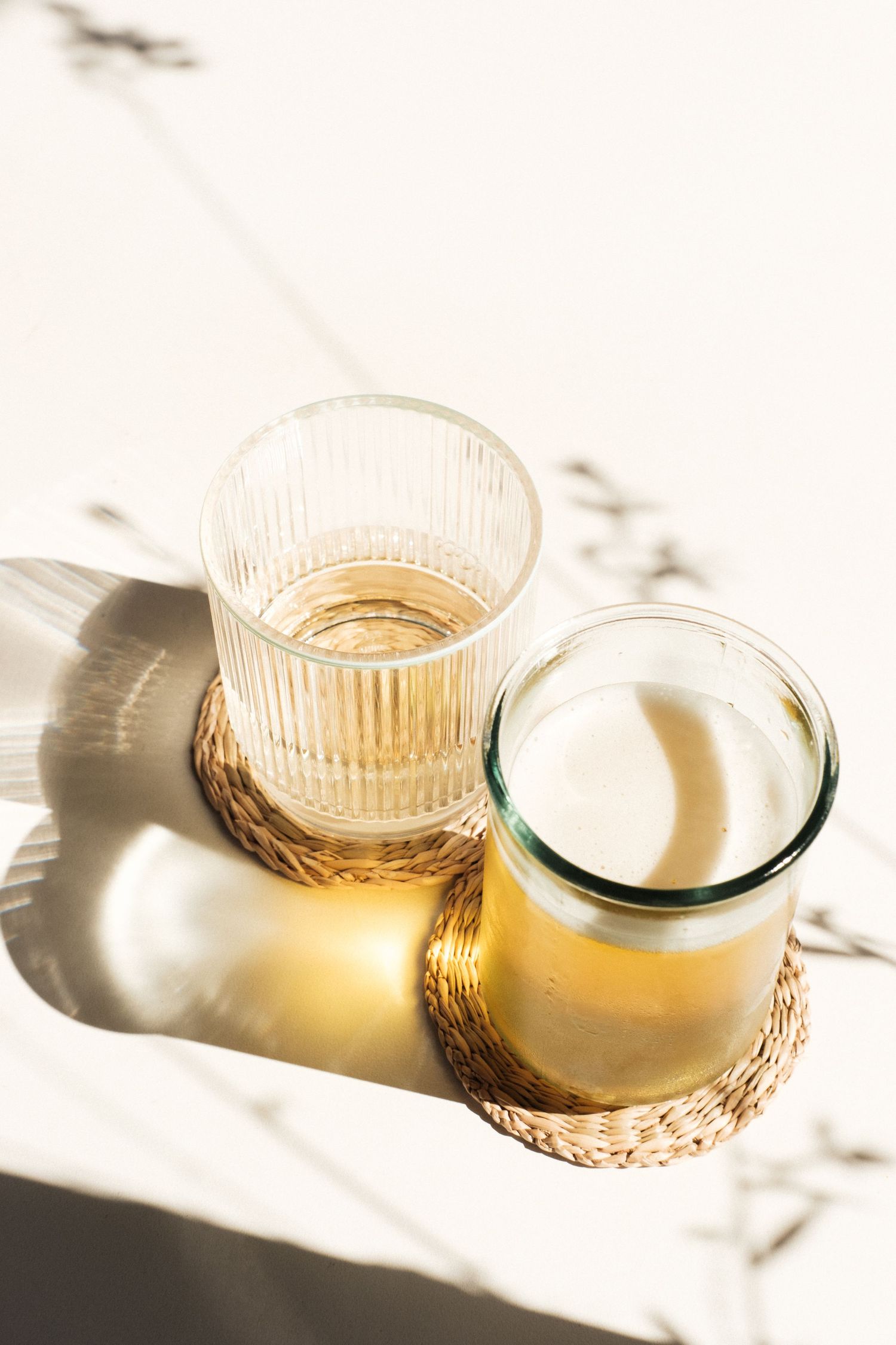 Amber and clear glass cups casting shadows on a white marble surface in sunlight.