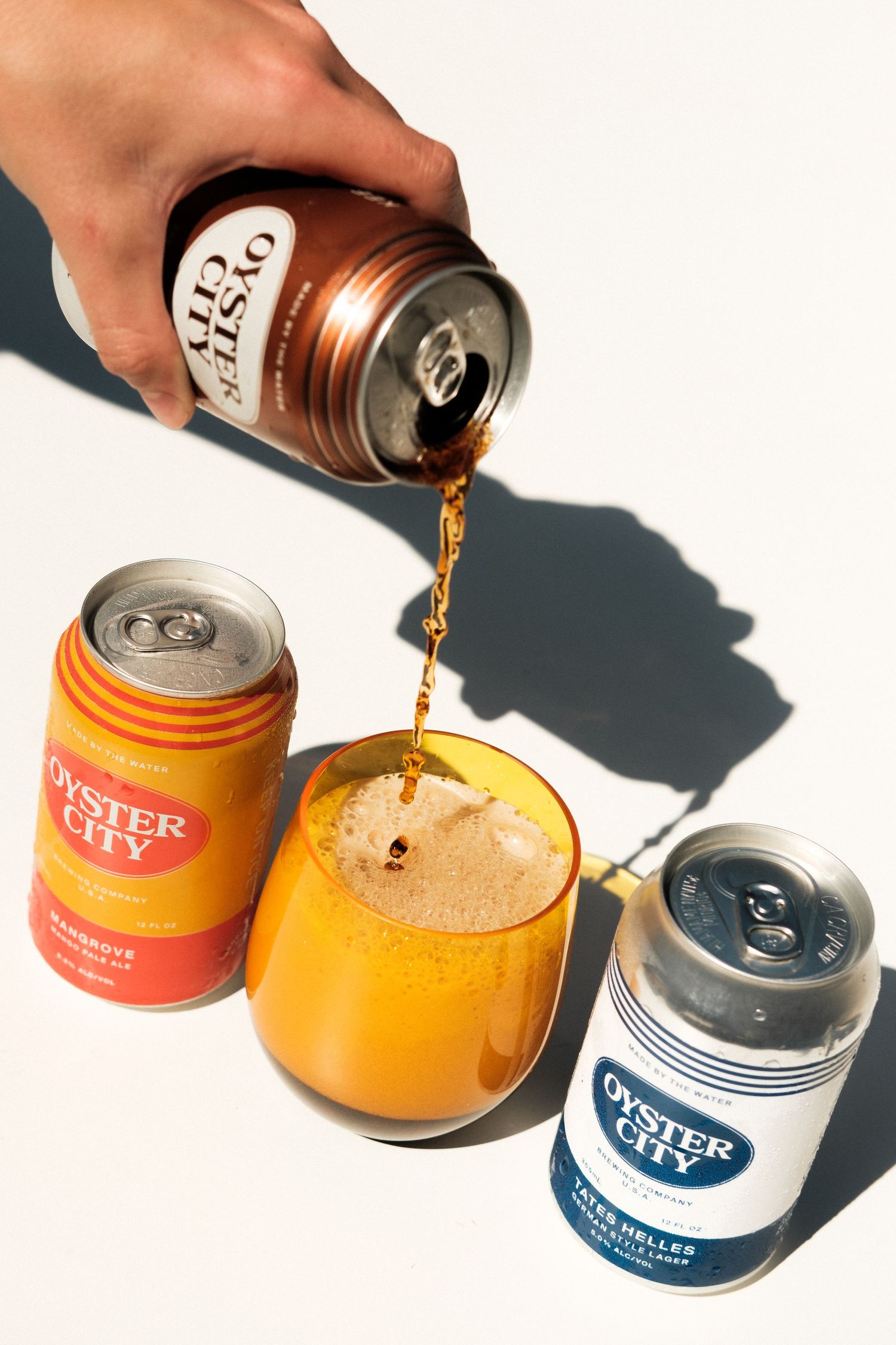 Liquid being poured into orange and blue cans in bright lighting against white background.