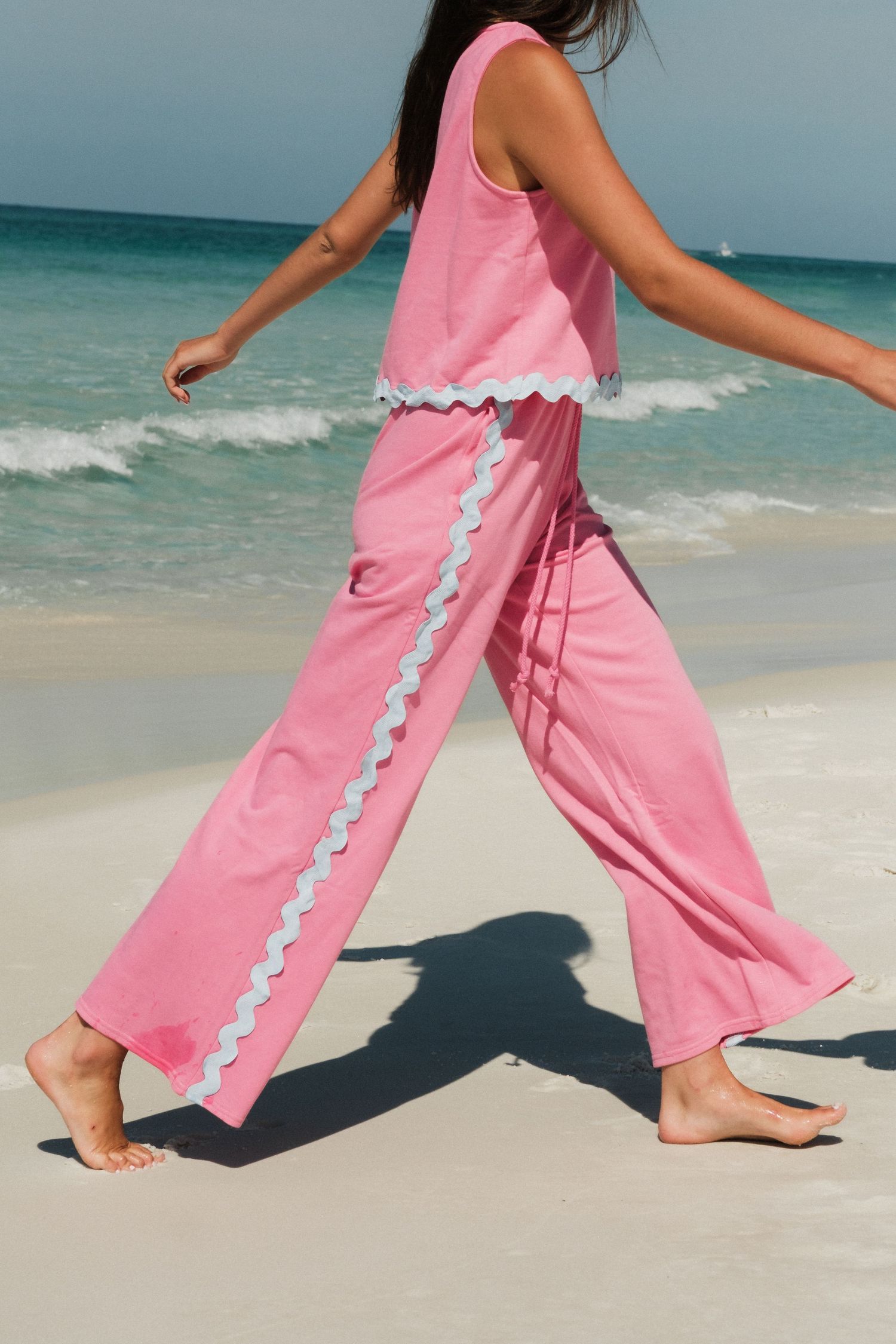 Close-up of pink beach pants with white trim walking on sandy beach.