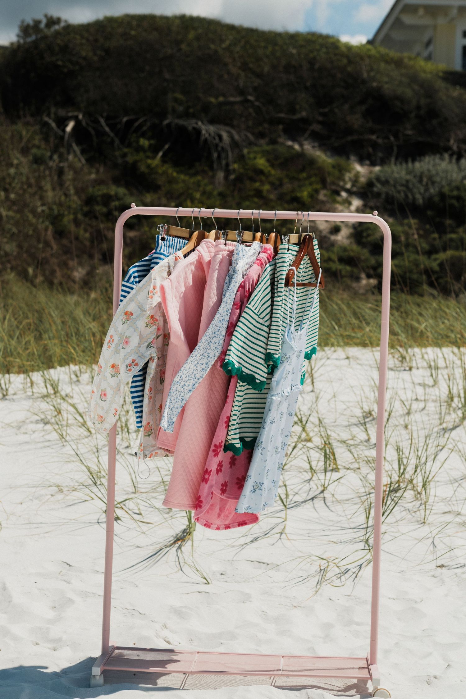 Pink clothing rack with striped and pastel garments on white sand dunes.