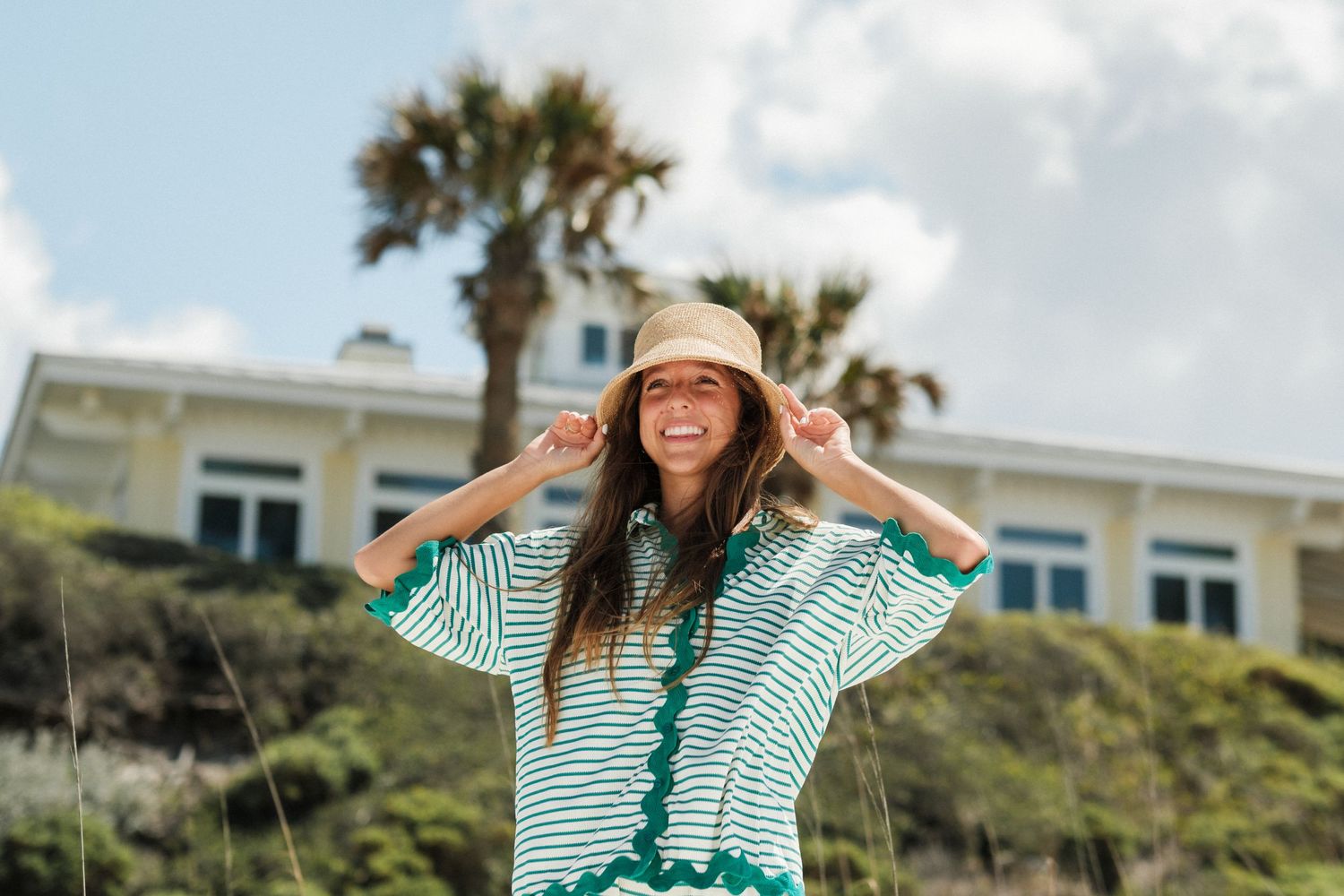Striped beachwear and sun hat against coastal scenery with palm trees.