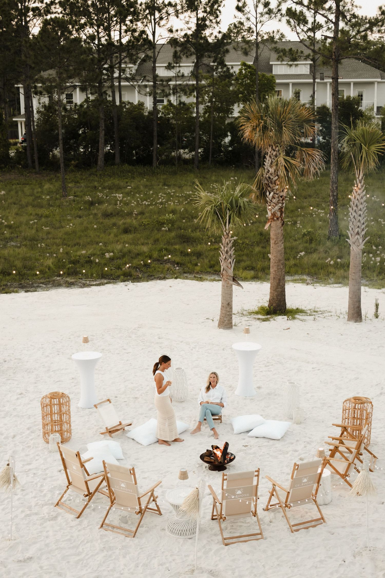 Beach setup with wooden lounge chairs and white cushions arranged on white sand.