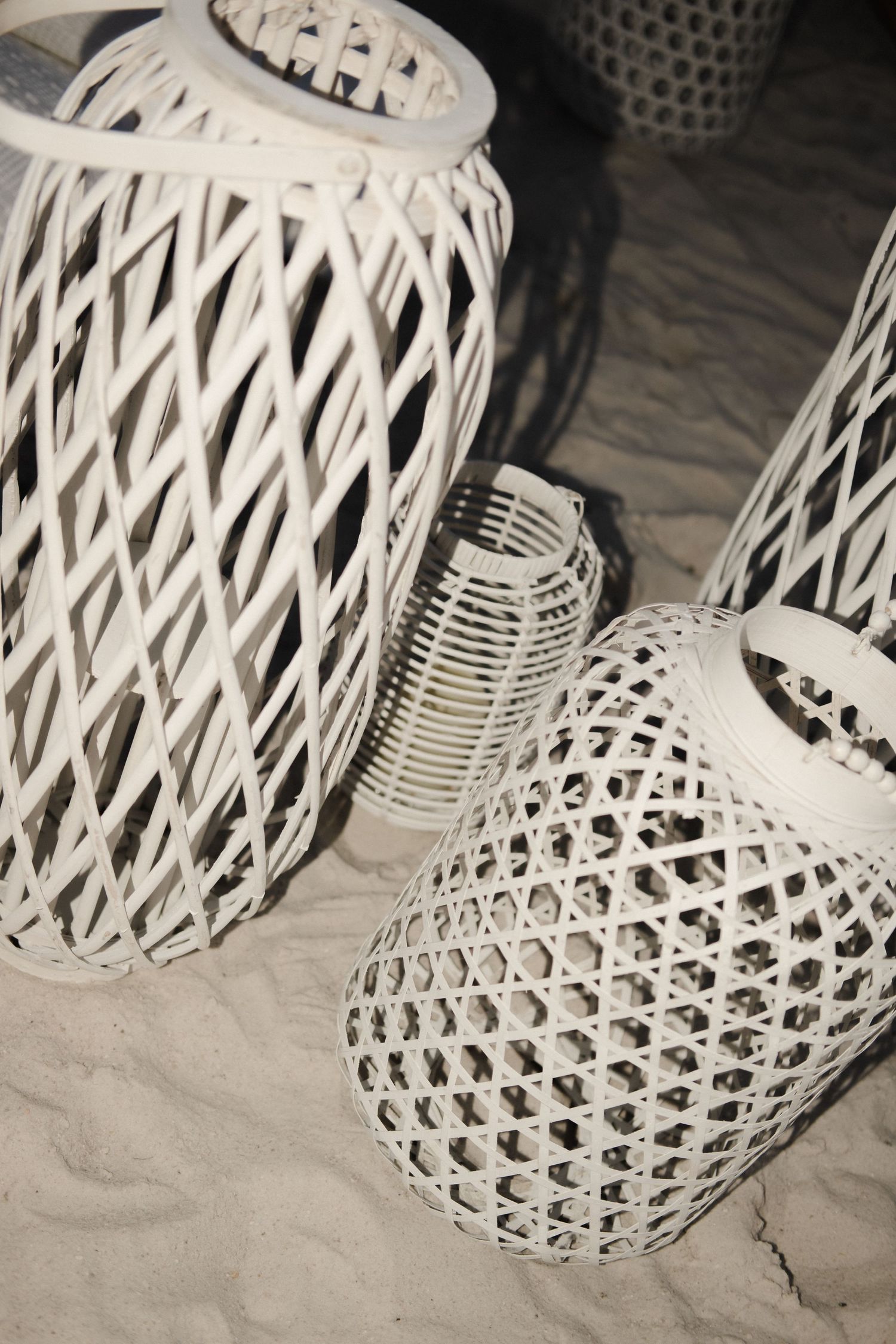 White woven lanterns create an elegant beach decor display on sand.