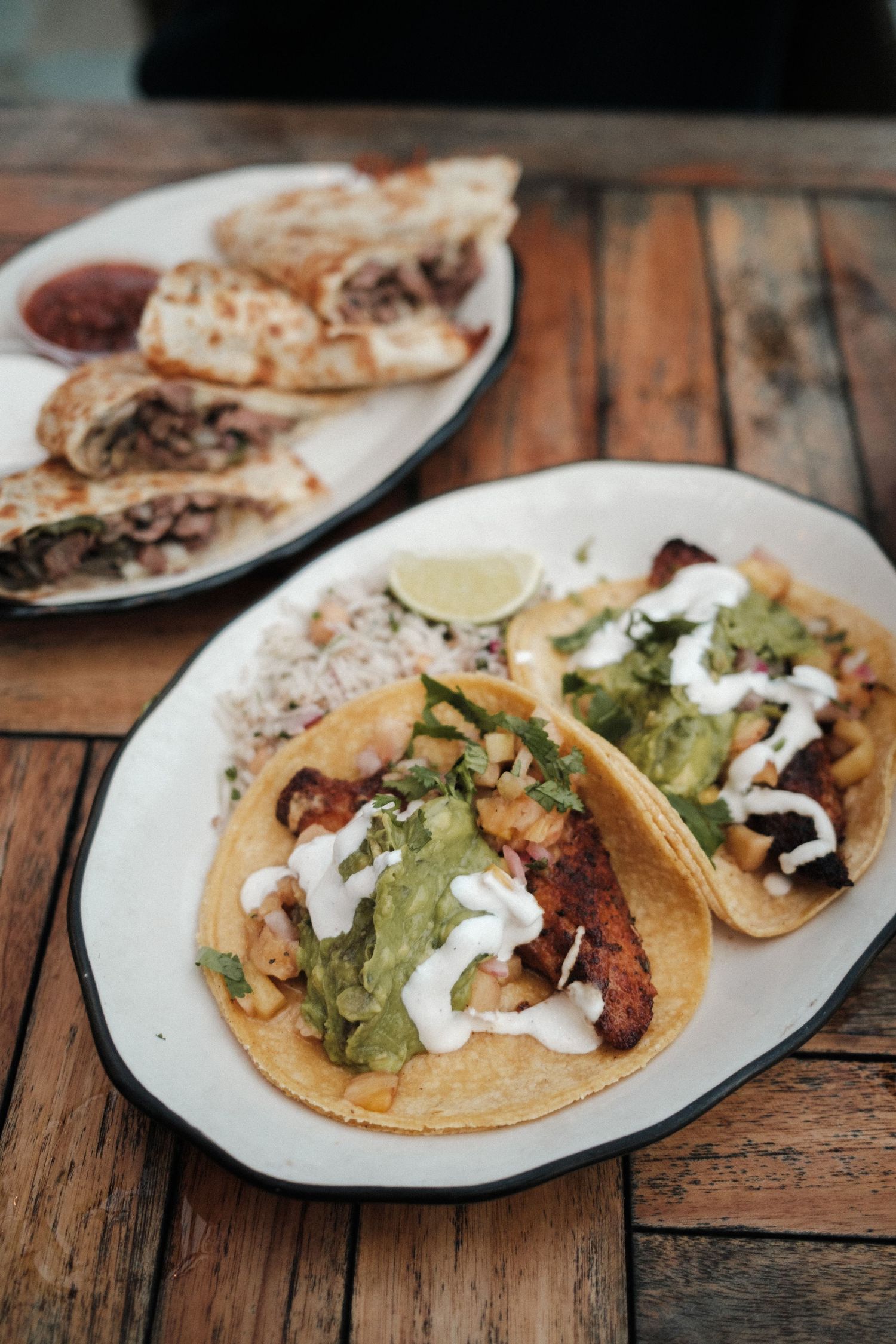 Plate of authentic Mexican tacos with guacamole and sour cream on wooden table.