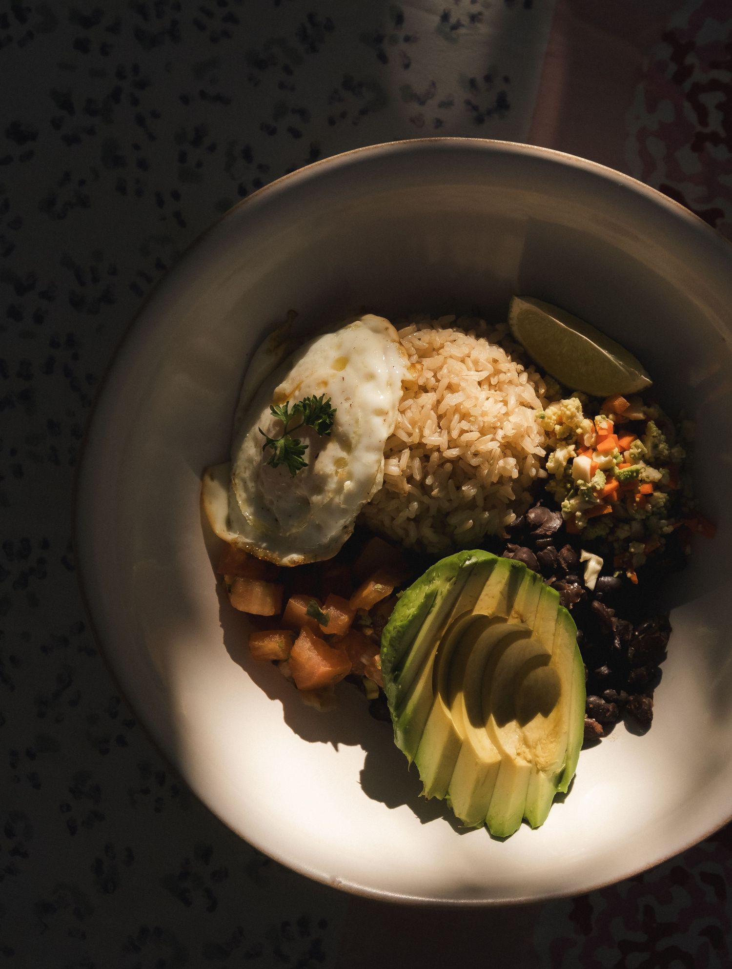 Healthy bowl with avocado slices, grains and greens in dramatic lighting.