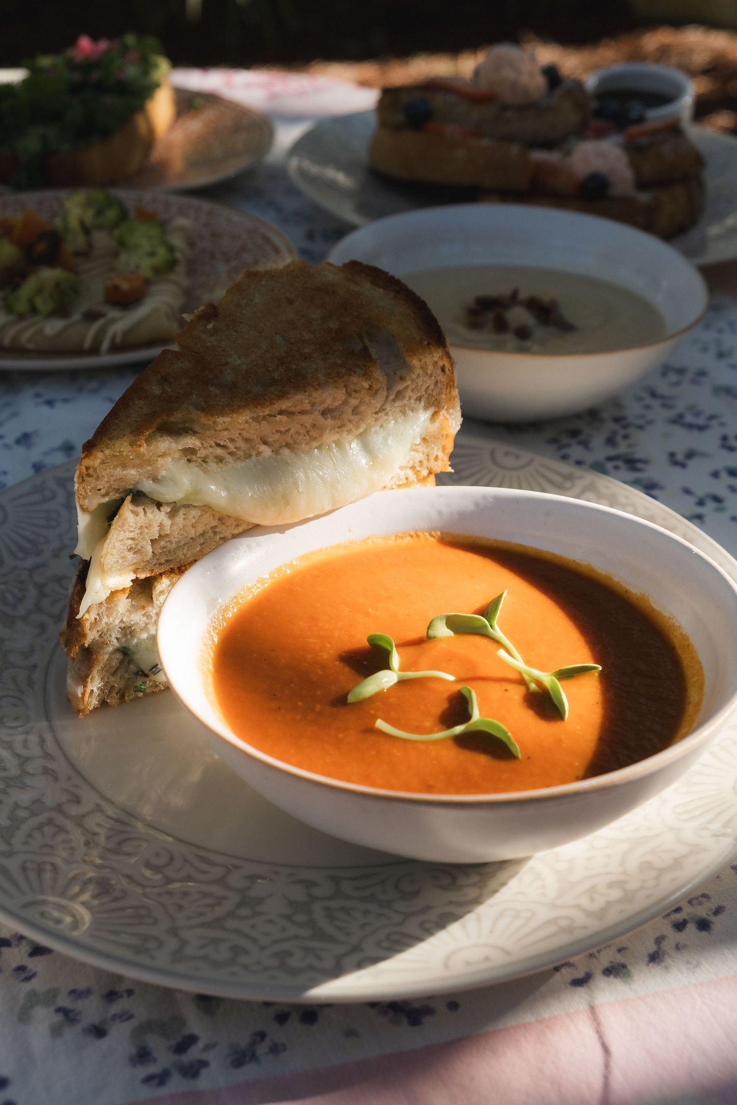 Creamy tomato soup served in white bowls with crusty bread on a patterned tablecloth.