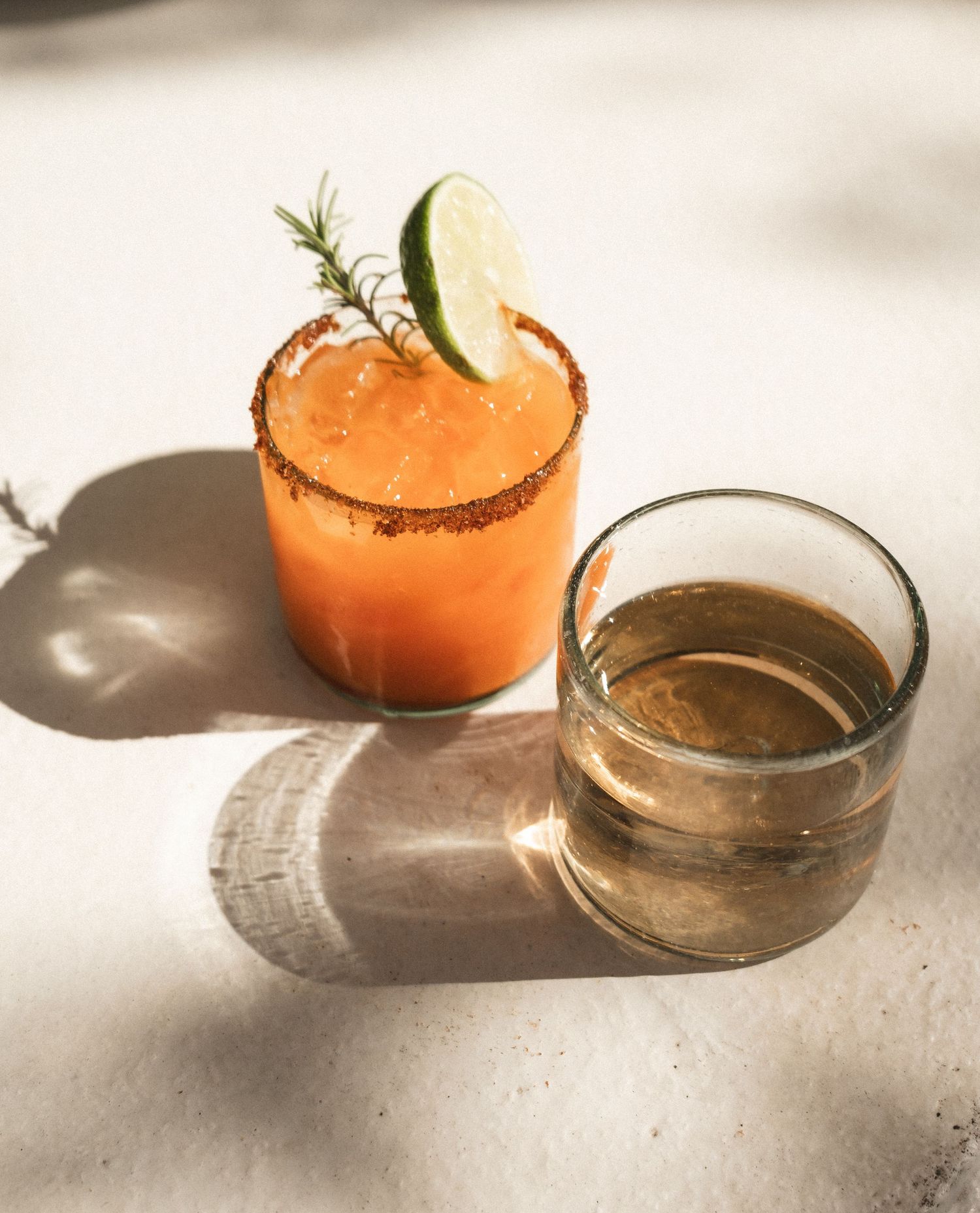 Orange citrus cocktail garnished with lime in a small glass bowl.