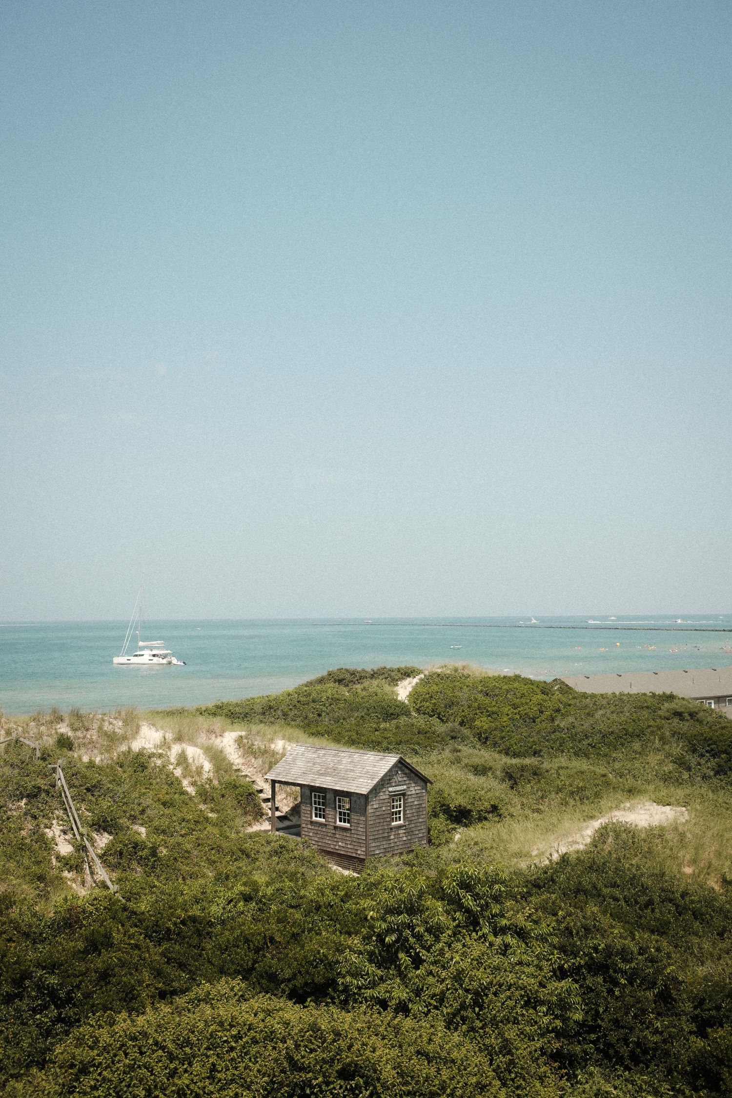 Coastal landscape with small cottages nestled among green dunes and a boat visible in the turquoise water.
