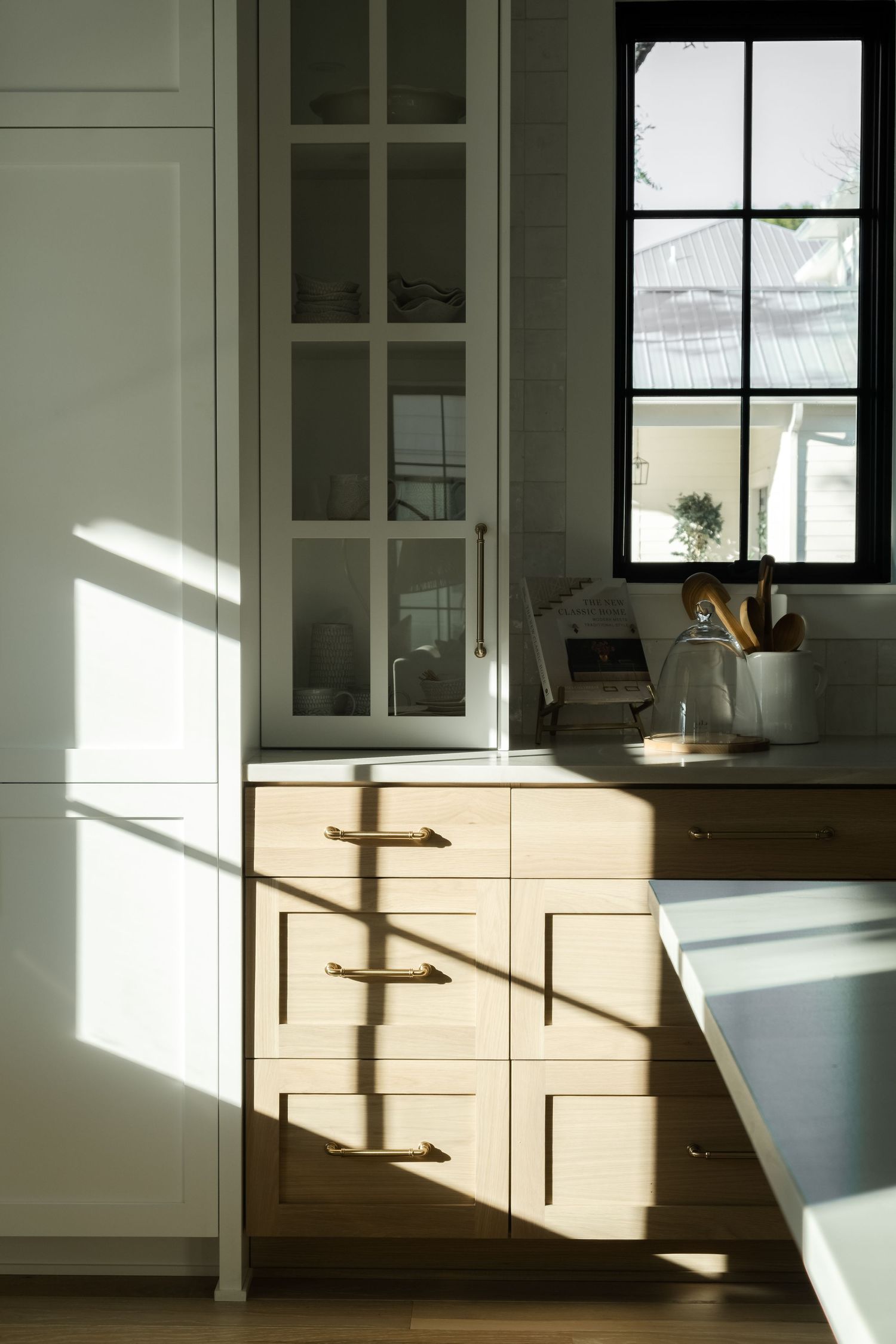 Sunlight casting dramatic shadows across white kitchen cabinets.