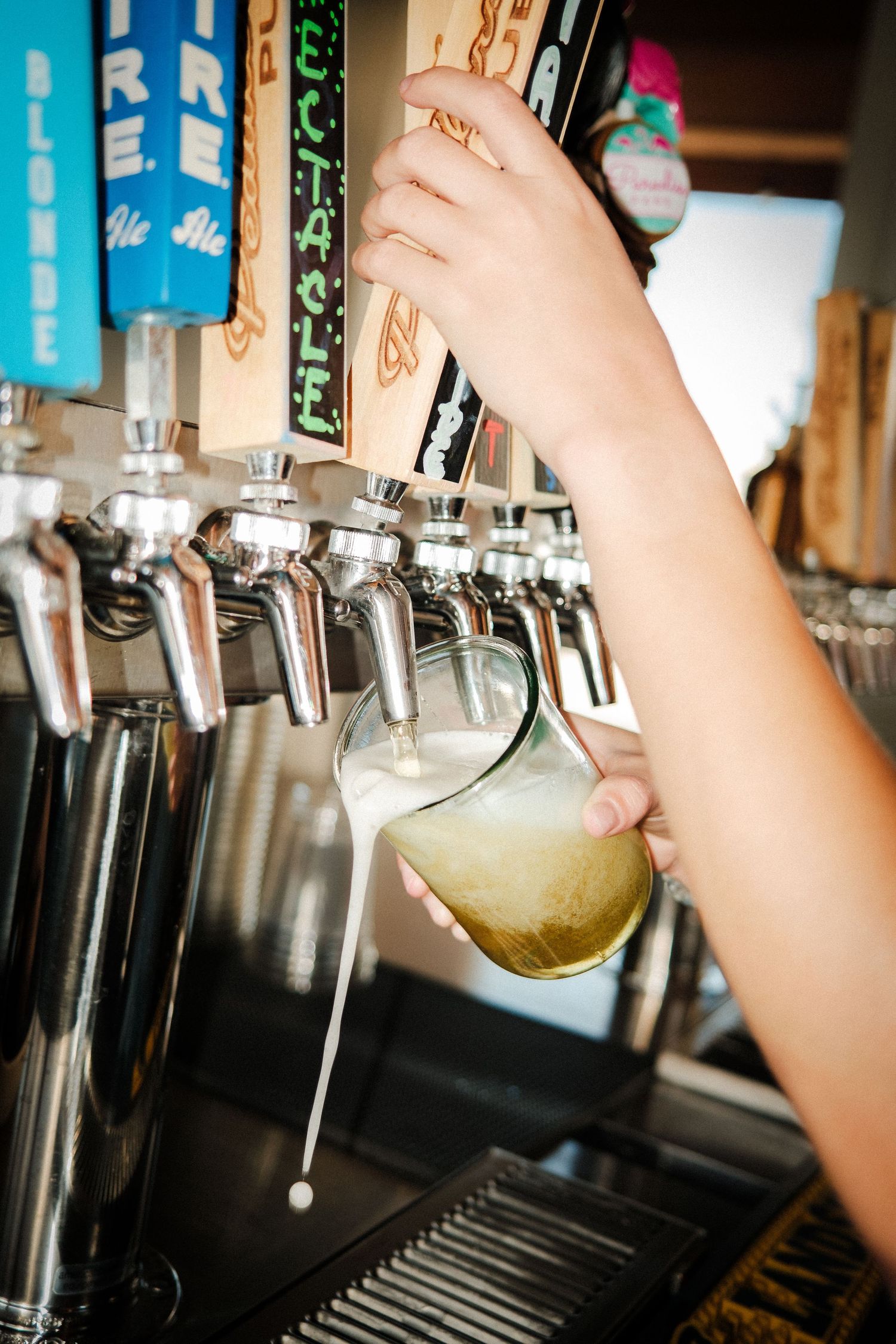Beer taps at a bar being operated to pour draft beer.