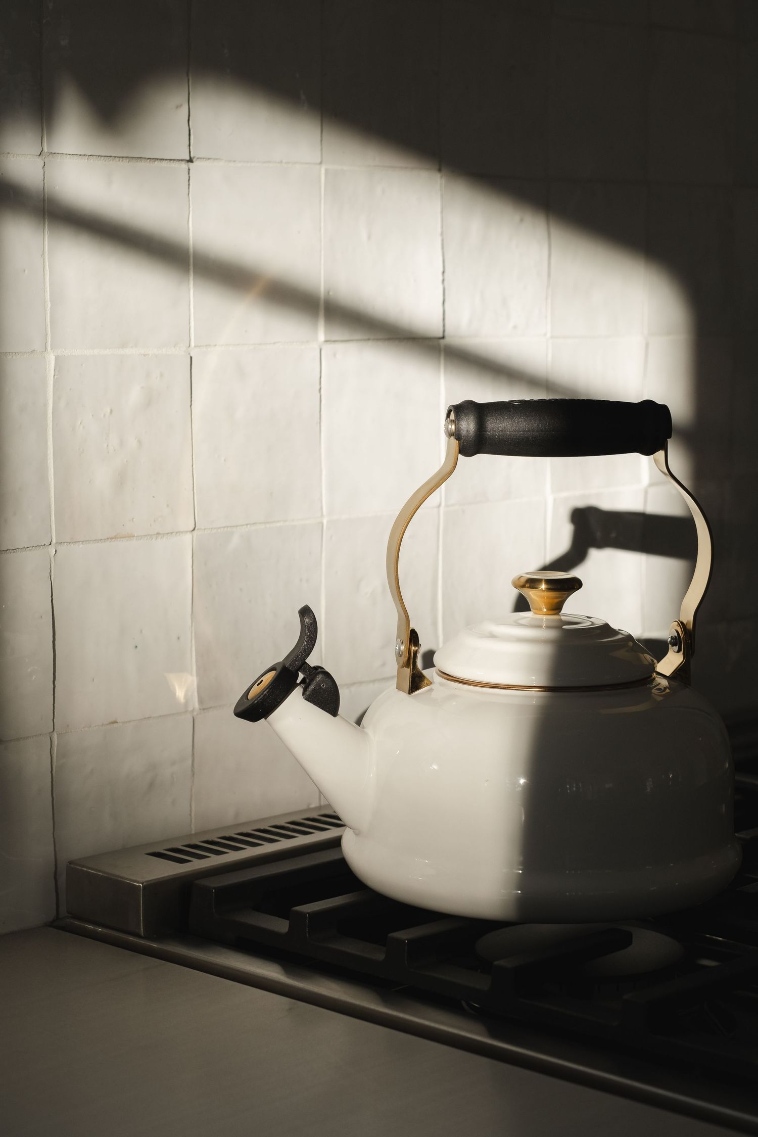 White kettle casting dramatic shadows on a tiled wall in moody lighting.