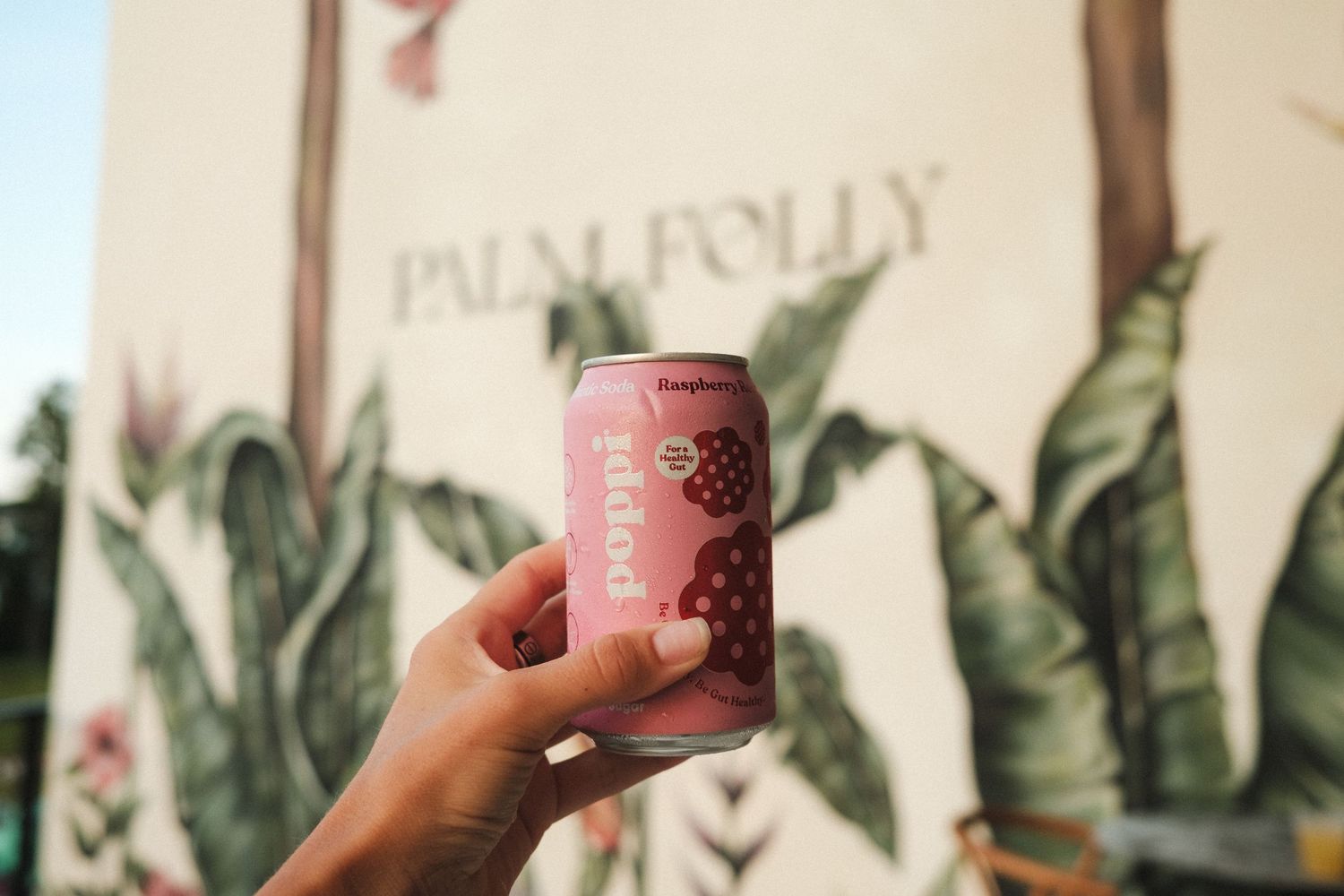 Hands holding branded pink drink cups against a tropical leaf backdrop.