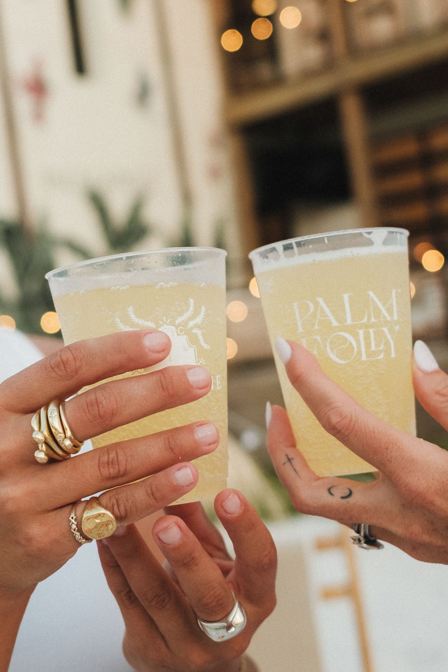Multiple hands toasting with branded Palm Folly cups in front of tropical decor.