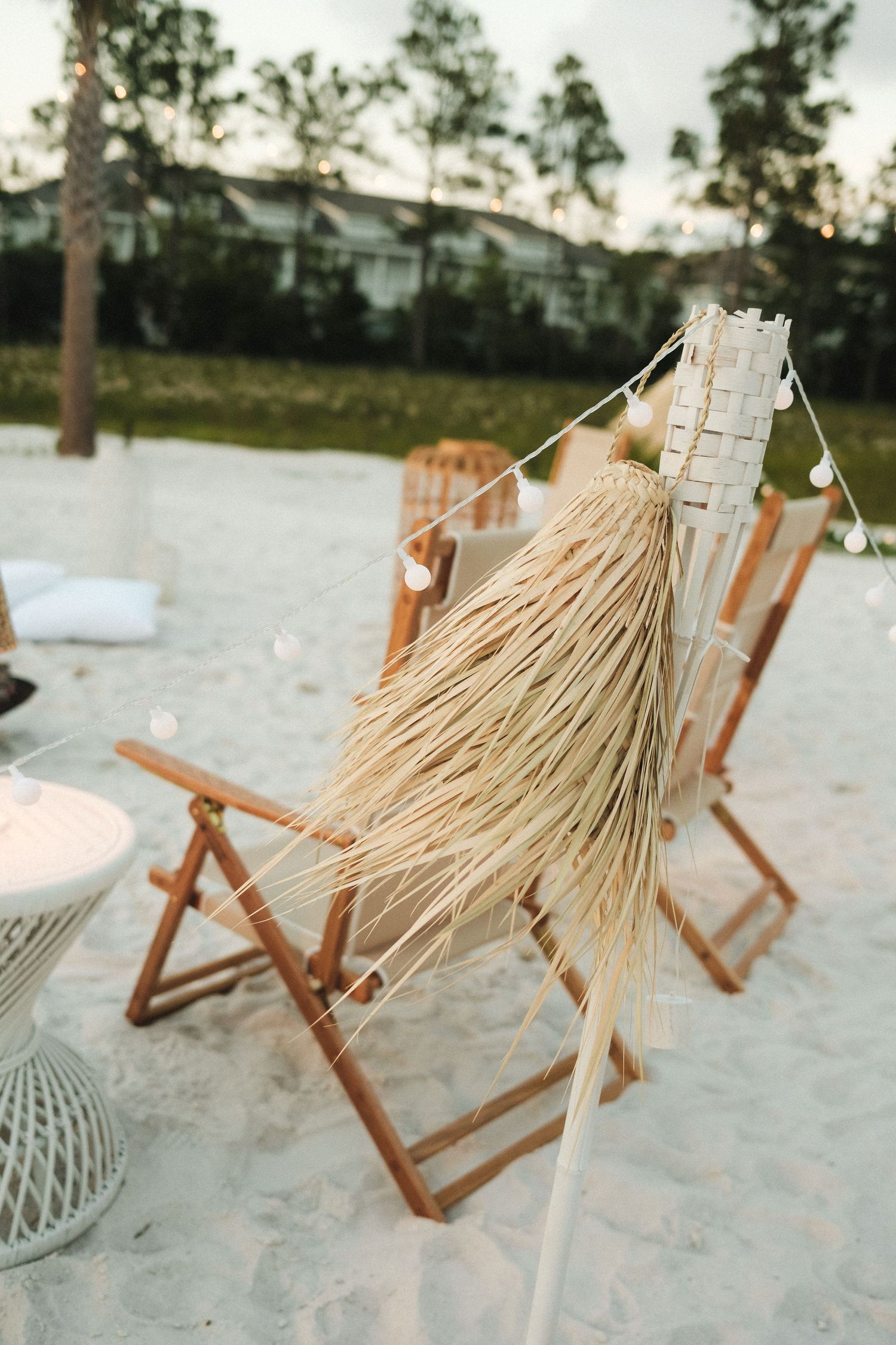 Wooden beach chairs and umbrellas line up on a sandy beach at sunset.