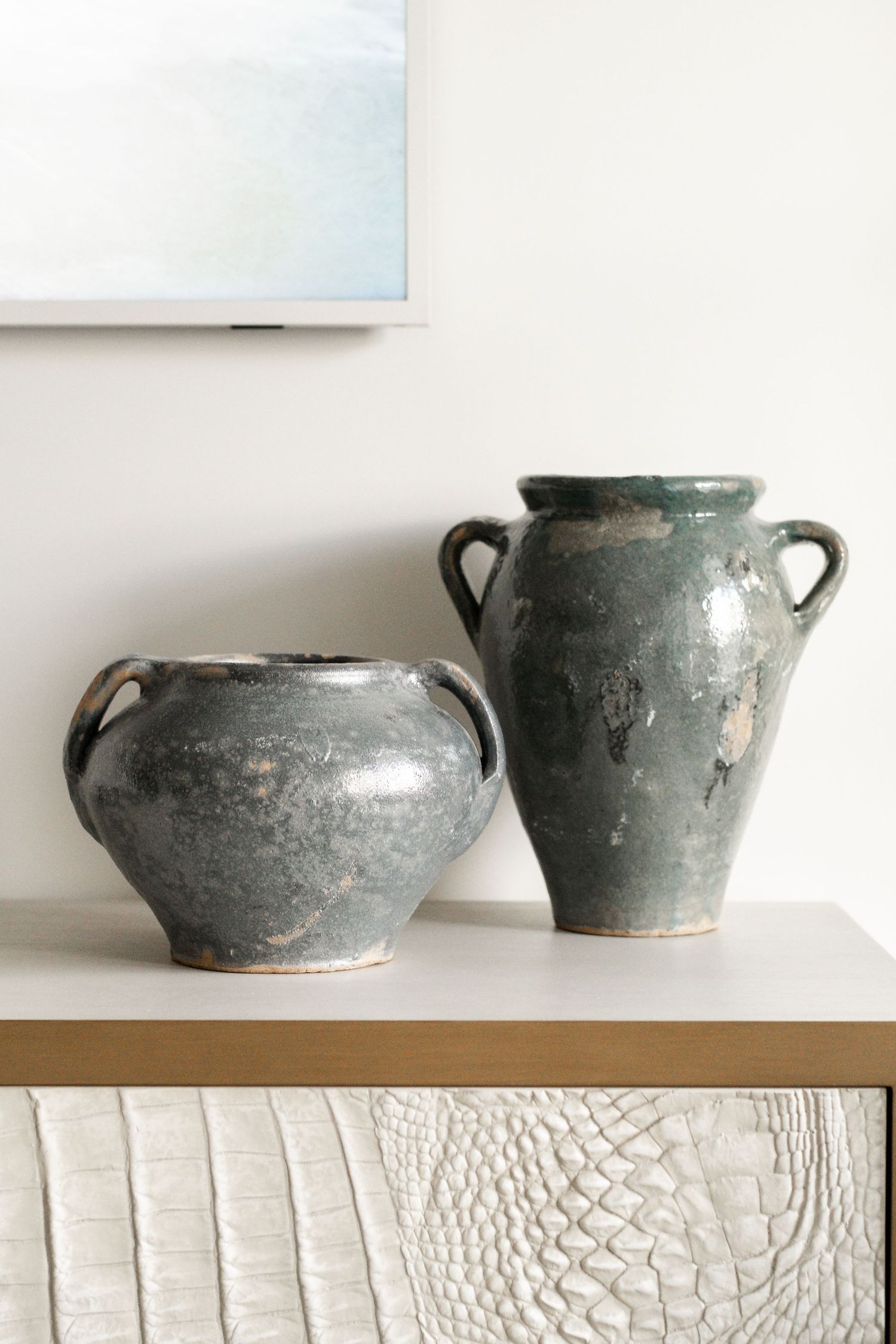 Collection of vintage gray ceramic pots displayed on a white shelf.