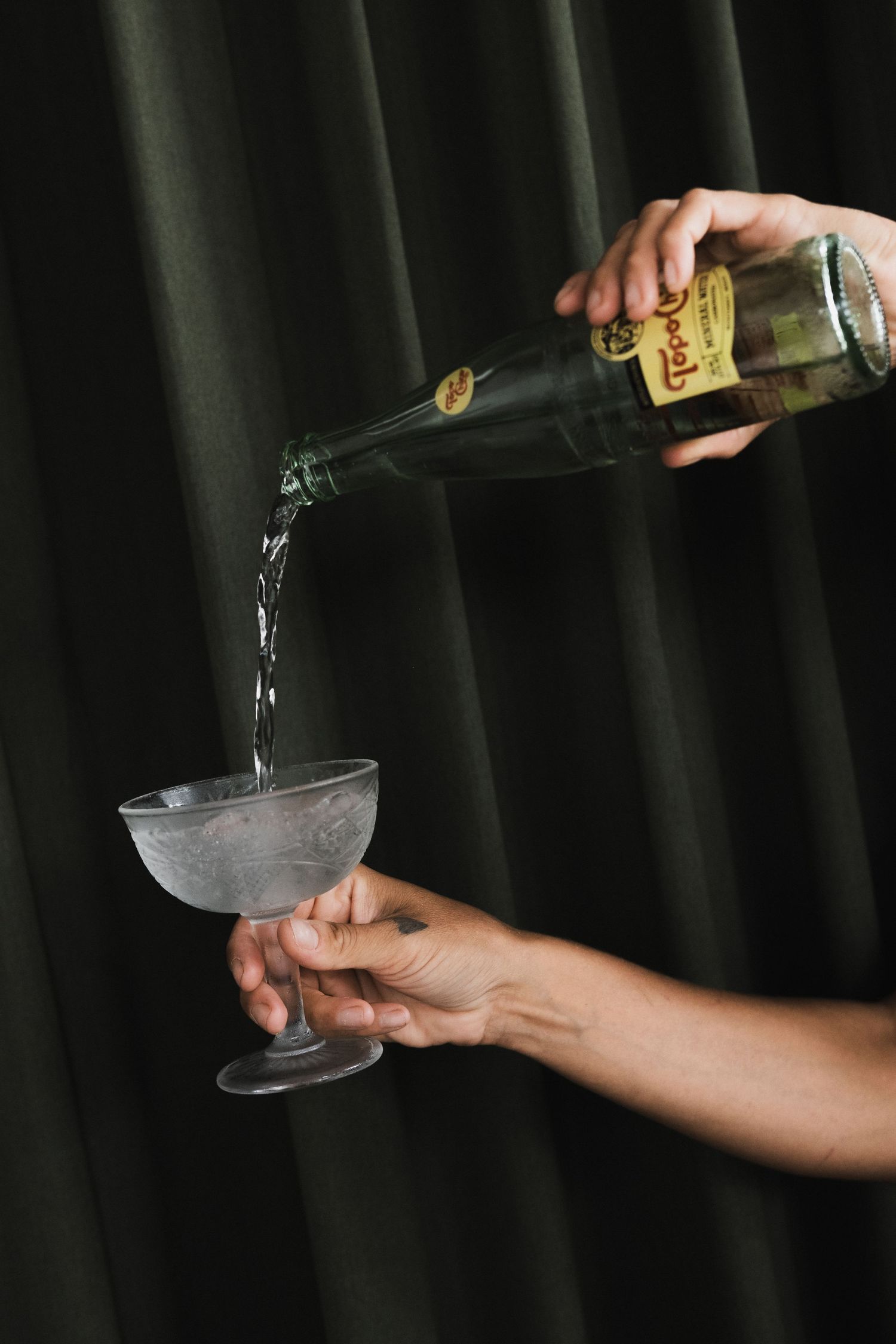Hands pouring champagne or sparkling wine into glasses against dark background.