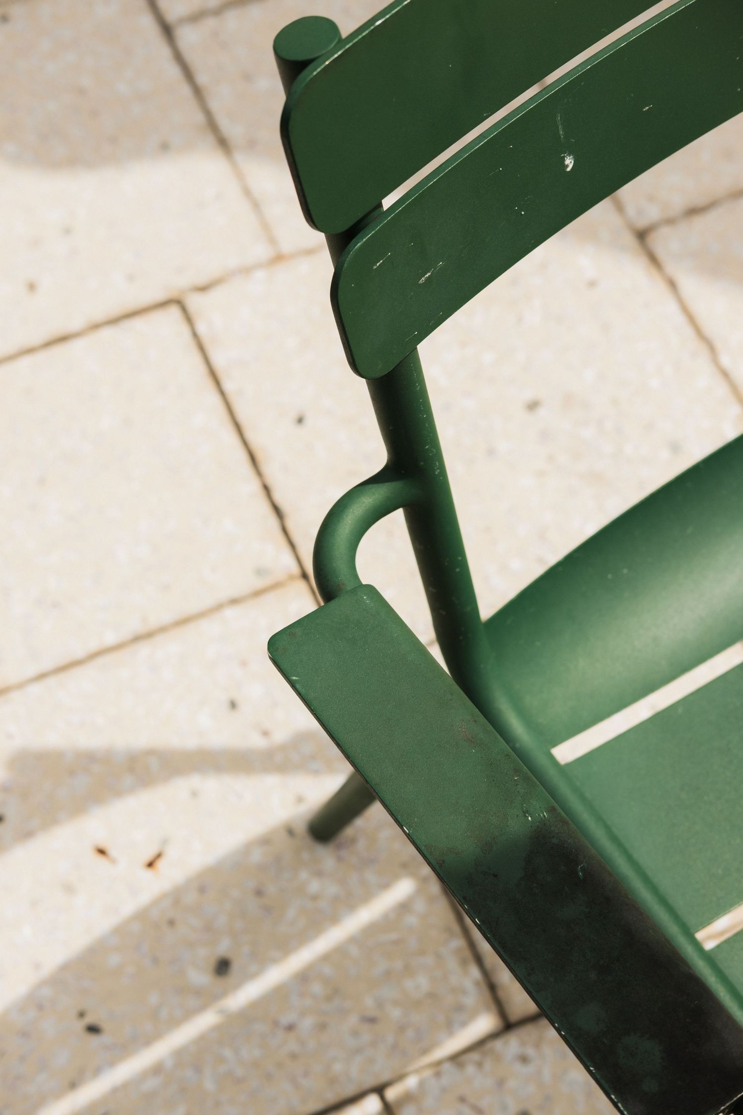 Close-up details of a green painted wooden chair in sunlight.