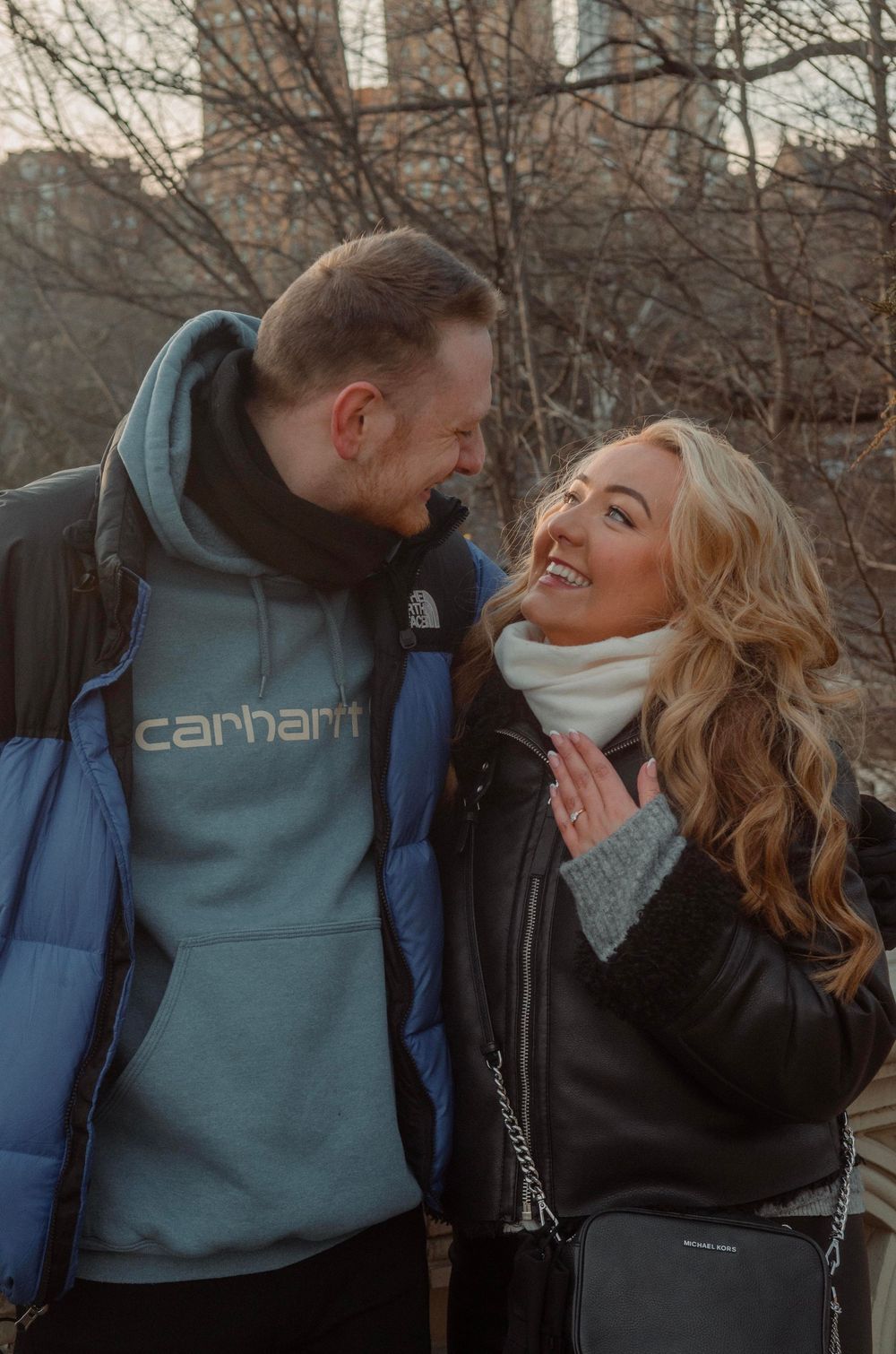 A couple shares a joyful moment together outdoors on a winter day, wearing warm coats and smiling at each other.