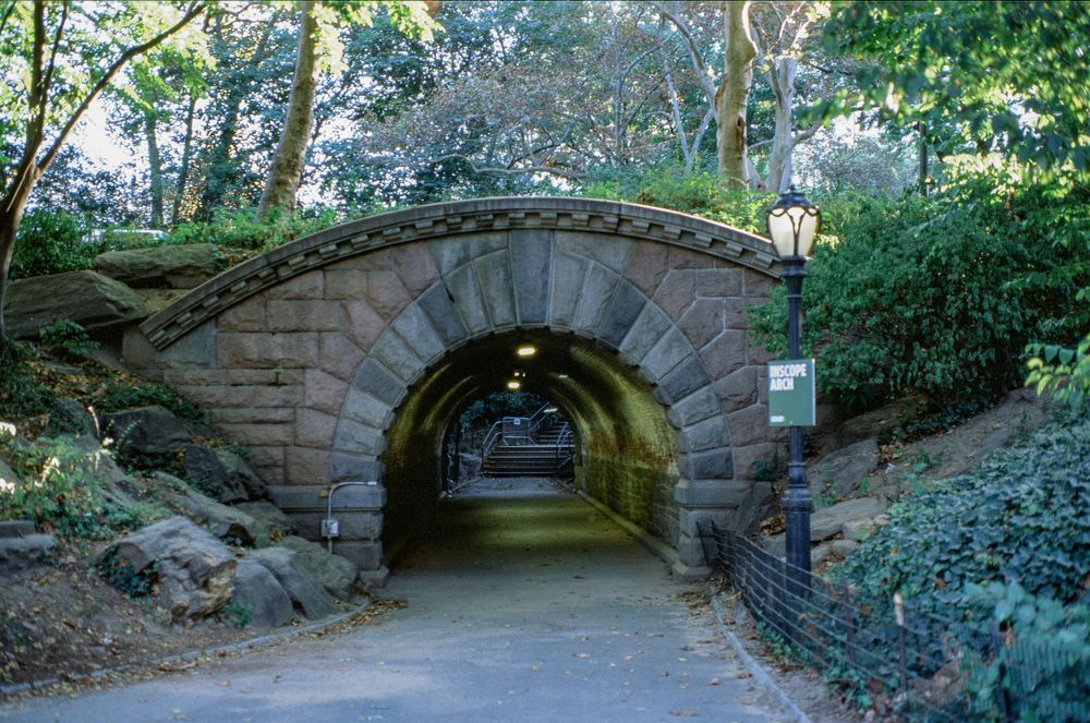 Stone tunnel archway illuminated at dusk in Central Park with vintage lampposts.
