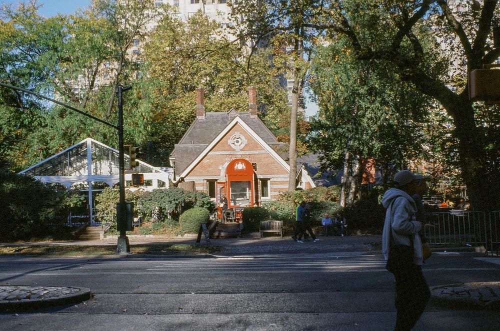 Small cottage-style building with orange door nestled among trees on a residential street.