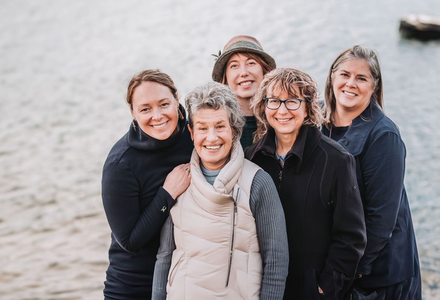 A group of people laughing and embracing while sitting together outdoors on a sandy beach.