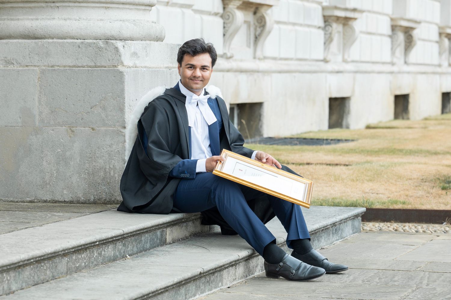 Professional in navy suit sits casually on concrete steps while reading documents in an outdoor setting.