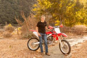 Person stands beside red dirt bike motorcycle in desert landscape.
