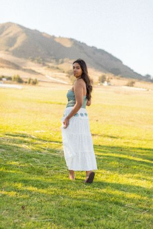 A serene portrait against rolling hills featuring a white tiered dress and blue top.
