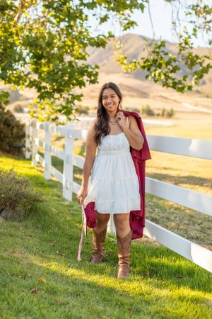 A countryside portrait by a white fence featuring a white sundress and brown boots in warm afternoon light.