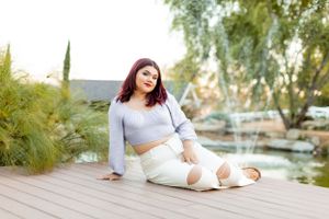 Woman in gray crop top relaxes on wooden deck by water feature.