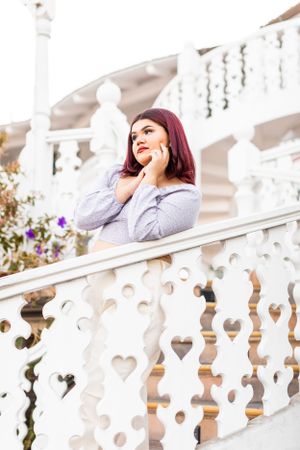 Woman in gray sweater poses on white ornate balcony with decorative railings.
