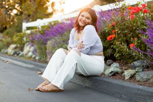 Woman in white outfit sits casually by colorful flower garden.