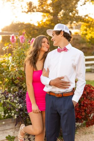 Couple shares romantic moment in garden with pink flowers and white fence.