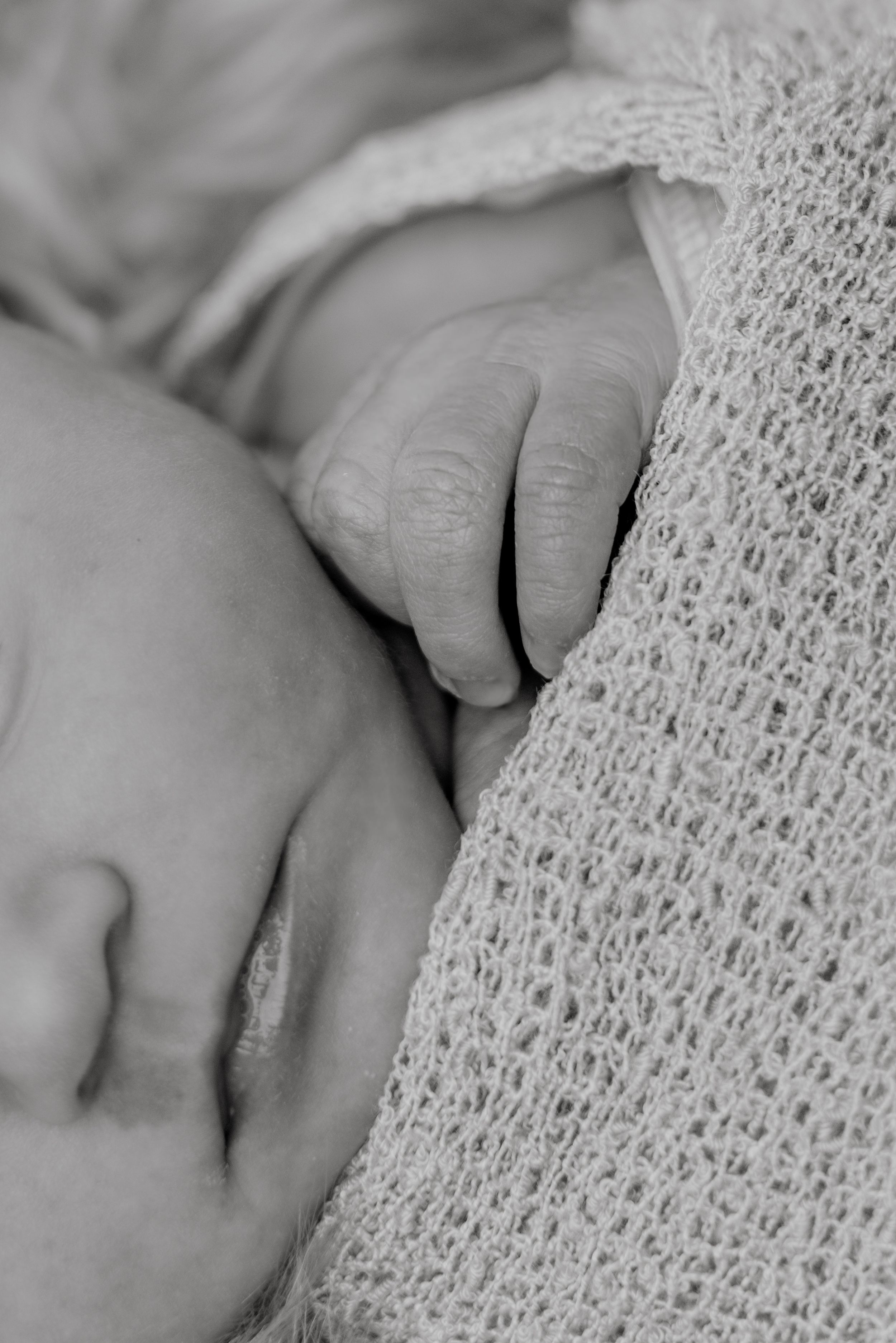 Close-up black and white photo of a tiny baby hand resting on soft knitted fabric.