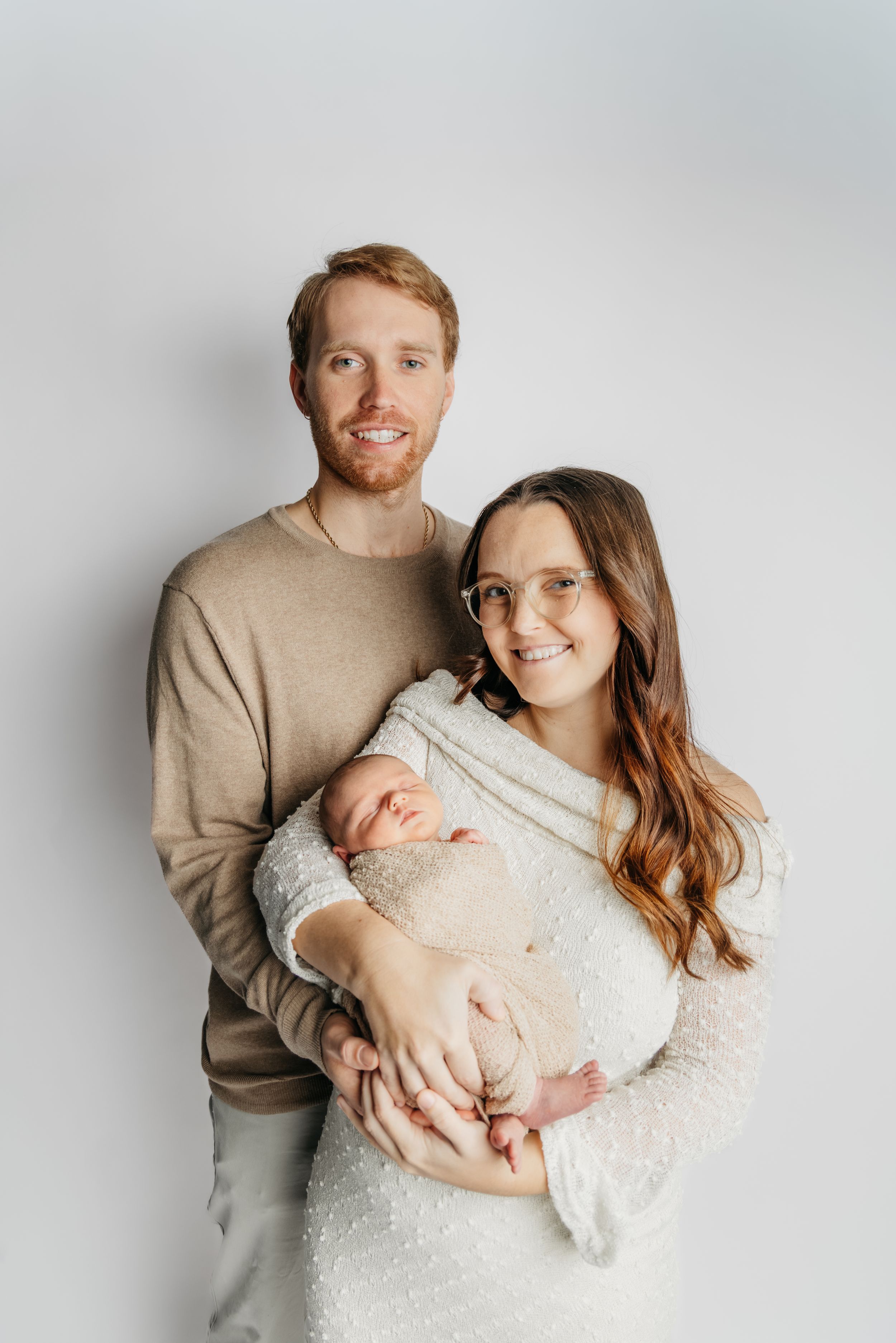 Sweet newborn photography session showing tender family moments against a light gray studio backdrop.