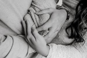 Black and white image of small hands holding each other against a textured blanket.