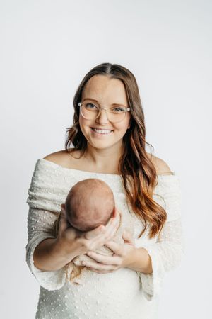 A woman in a white sweater holds a sleeping newborn baby against a white background in a series of tender poses.