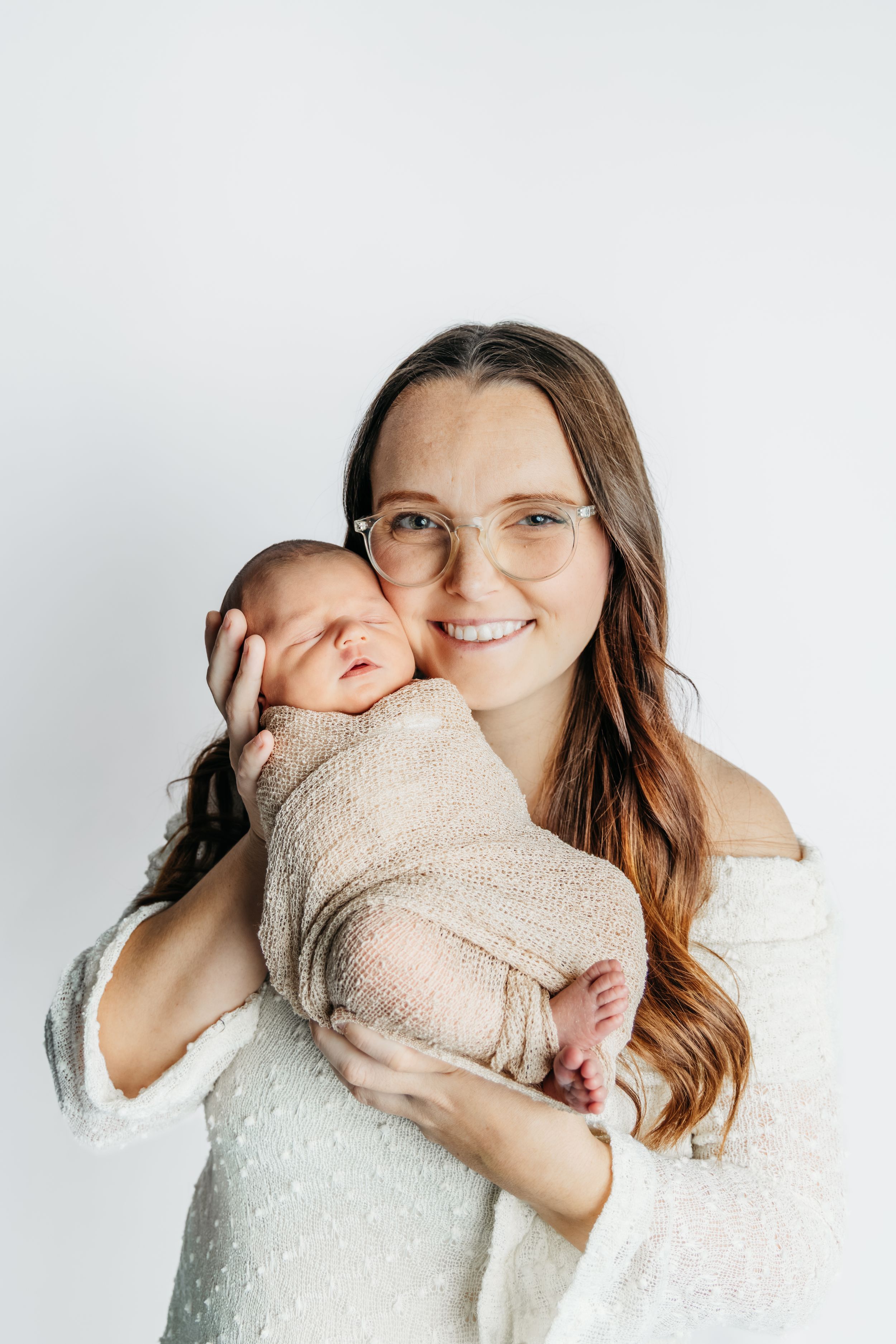 Intimate studio portraits of a mother holding her newborn baby wrapped in soft beige blankets.