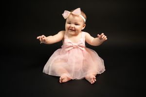 Baby wearing pink tulle dress against black background.