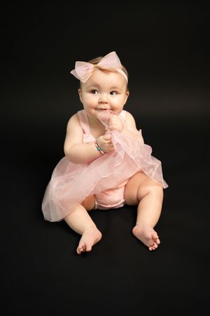 Baby in pink tulle dress and bow lying on black backdrop.