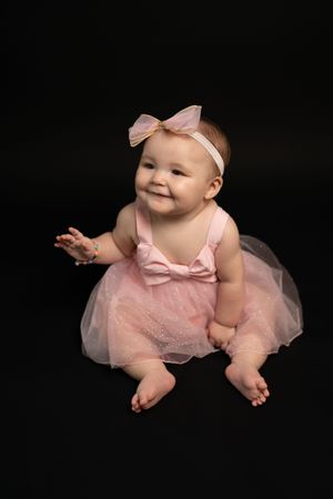 Smiling baby in pink tutu dress against dark background.