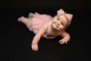 Happy baby in pink dress posing on black background.