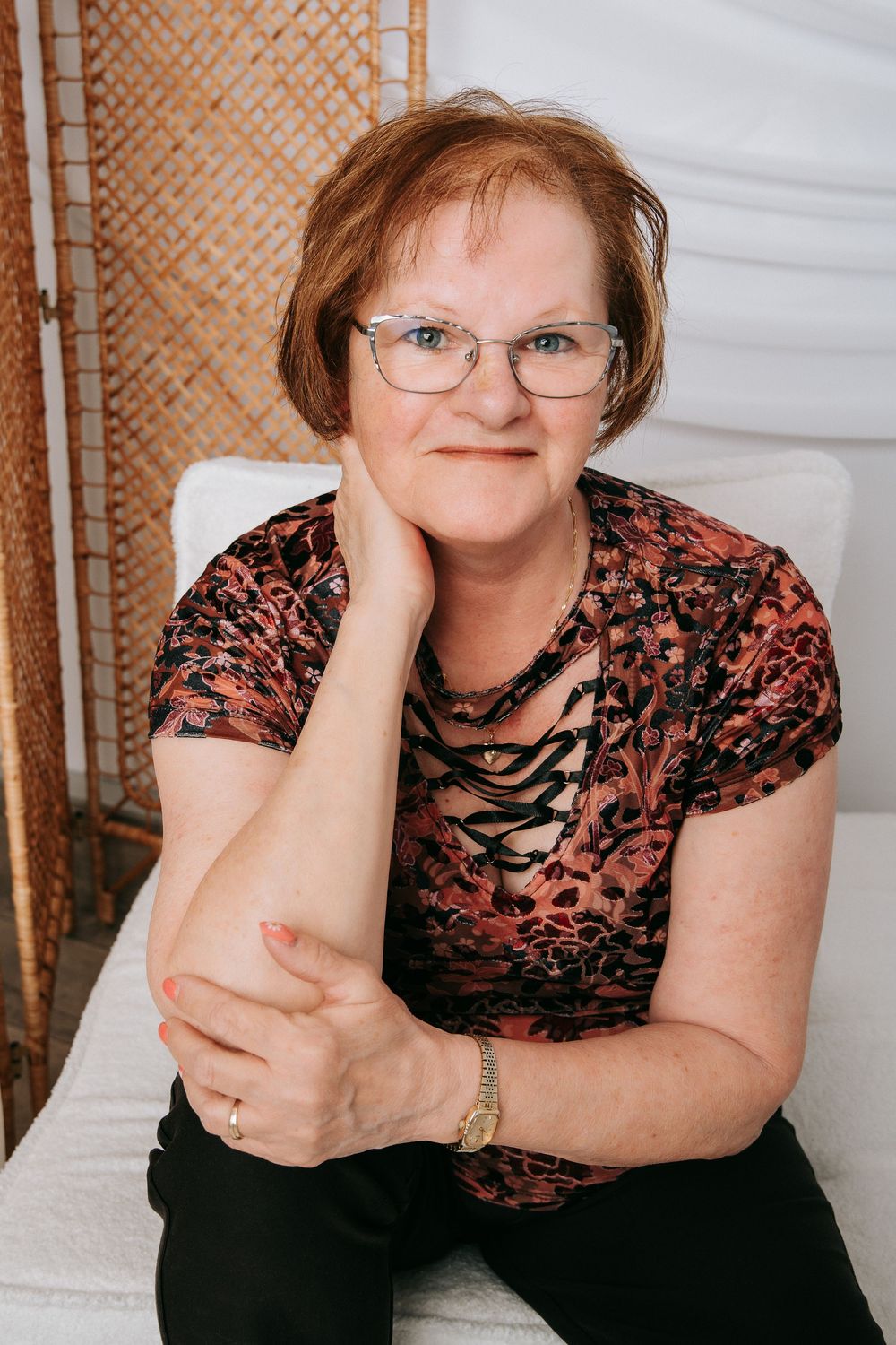A person in glasses and a floral top poses in three similar shots while sitting and leaning on a surface.