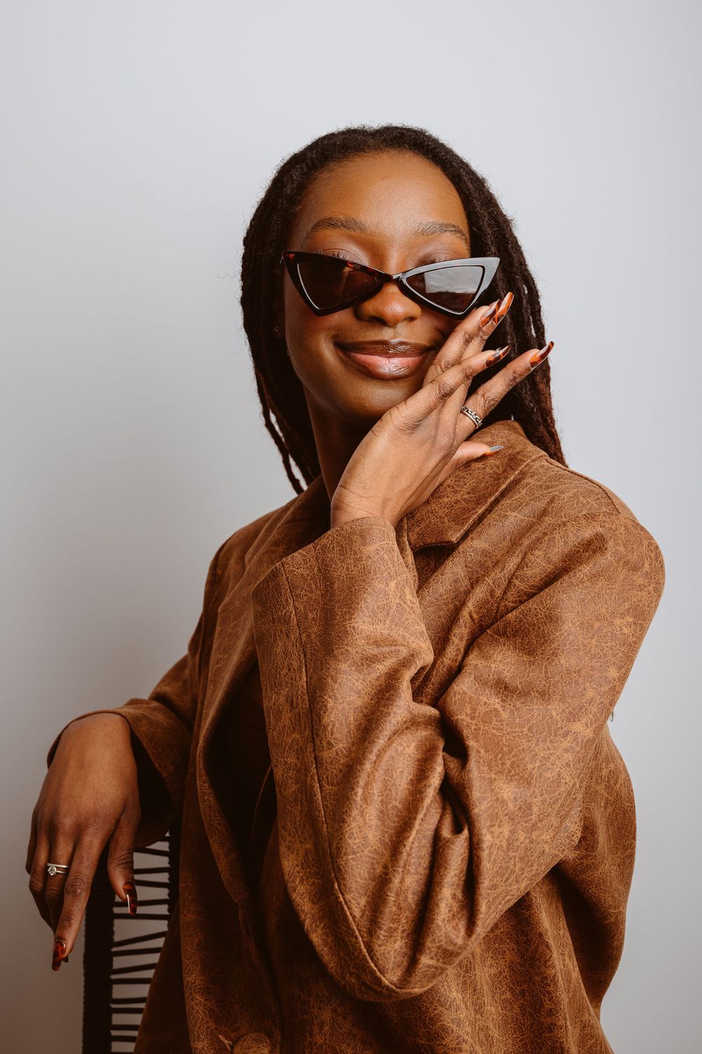 A series of candid shots showing someone in a brown coat and sunglasses expressing joy and laughter against a light background.