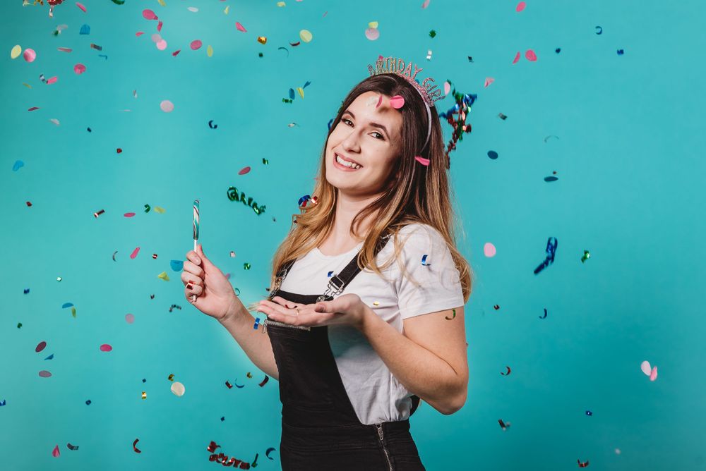 Person celebrating with confetti against turquoise background while holding party accessories.
