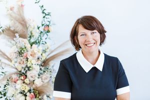 Professional wearing a black and white collared outfit stands against a bright floral backdrop.
