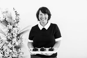 Person in black and white uniform smiles while holding a serving tray against white background.