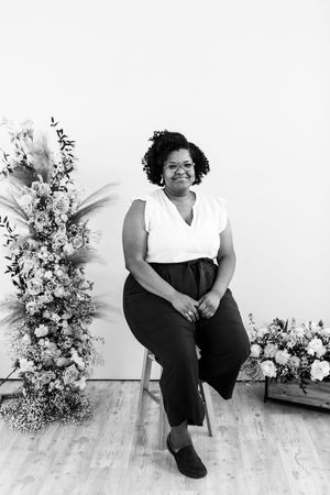 A casual portrait session with floral decorations and a person seated on a wooden stool against a white backdrop.