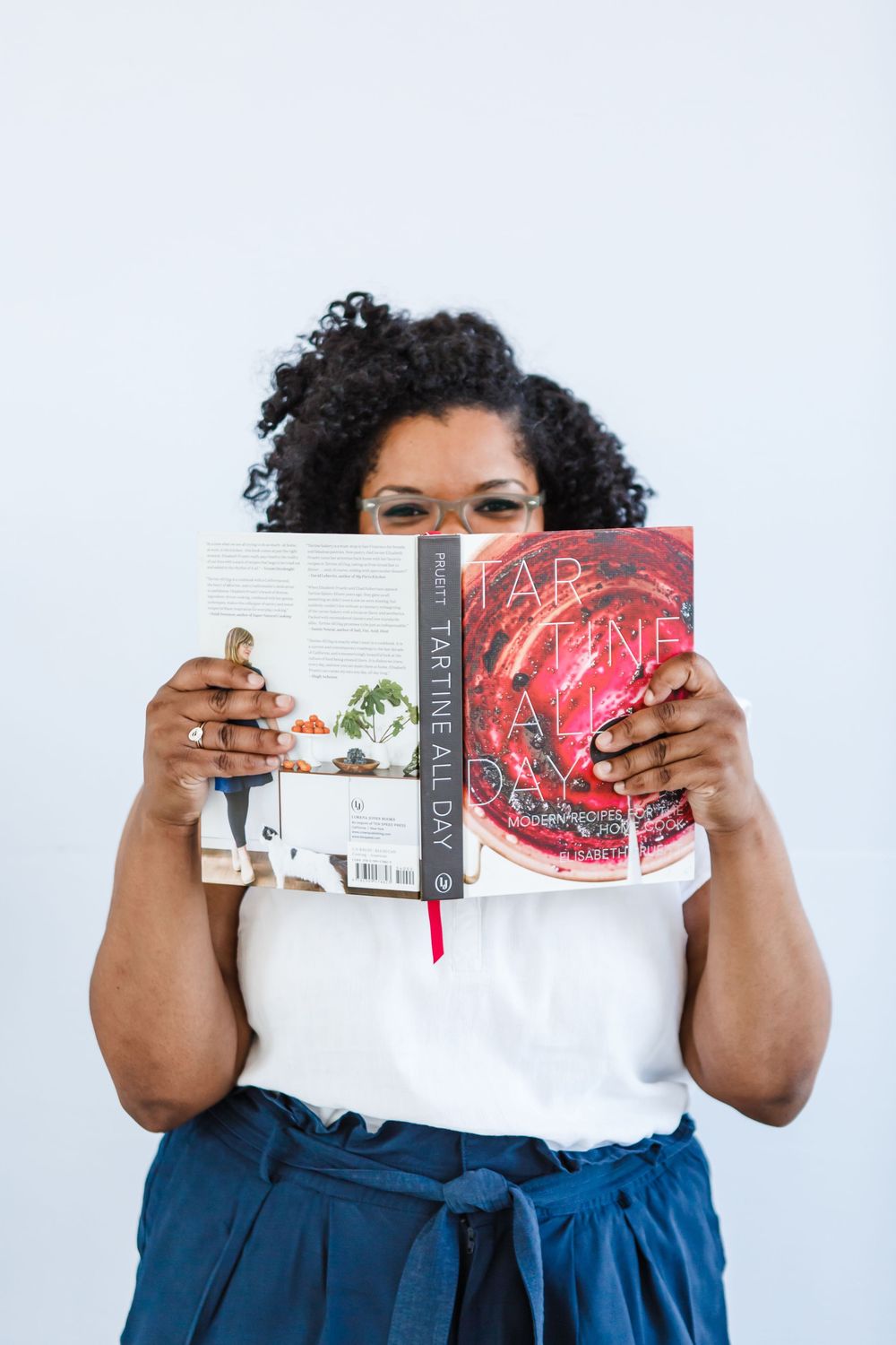 Hands holding open a red cookbook against a white background, showing pages inside.